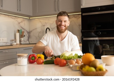 Young man sit at table and cut cucumber on salad