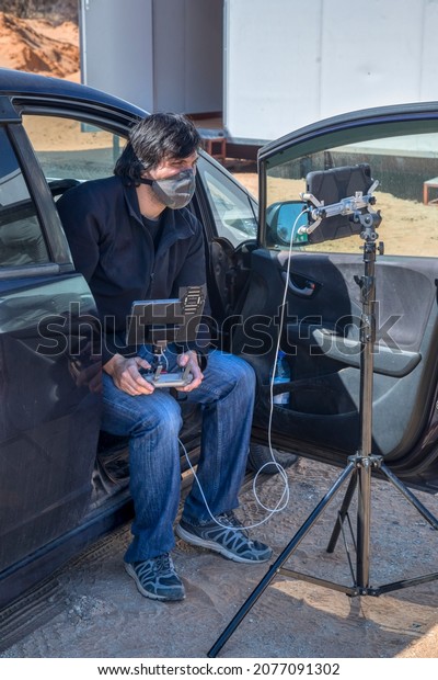 young man sited in the car holding a drone\
control and screens