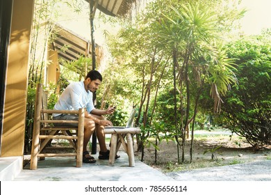 A Young Man Sits Near A Summer House On Vacation And Works At A Computer With A Phone In His Hand. Dream Work.