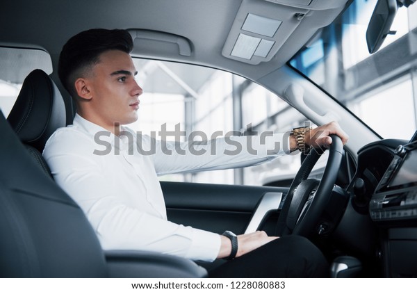 A young man sits in a newly purchased car at the\
wheel, a successful purchase