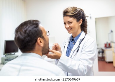 A Young Man Sits On An Exam Table Across From His Doctor. The Doctor Reaches Forward With A Tongue Depressor As The Man Looks Up And Sticks Out His Tongue.