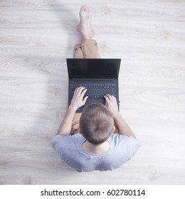 Young Man Sits On The Laminate Floor With Black Laptop. Top View