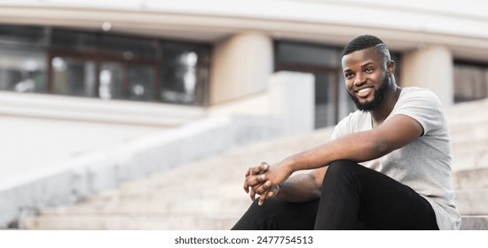 A young man sits on a set of city steps, smiling and looking off to the side. - Powered by Shutterstock