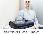 A young man sits in a psychological consultation while being treated with transcranial direct current stimulation. The machine is in the foreground. TDCS concept.