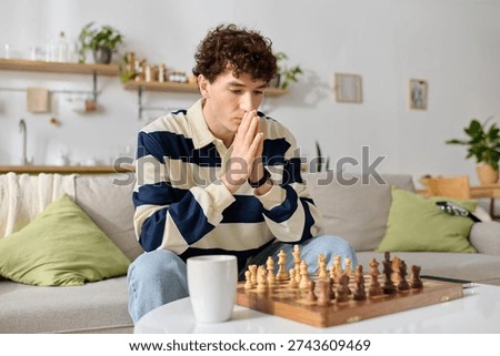A young man sits thoughtfully, analyzing his next move in a chess game on a cozy sofa.
