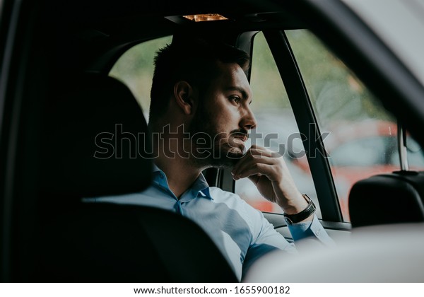 Young man sitting at the backseat looking out\
the window thinking