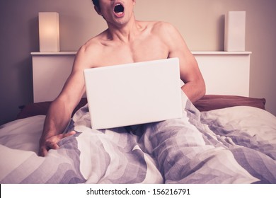 Young man is sitting in bed and watching pornography on laptop