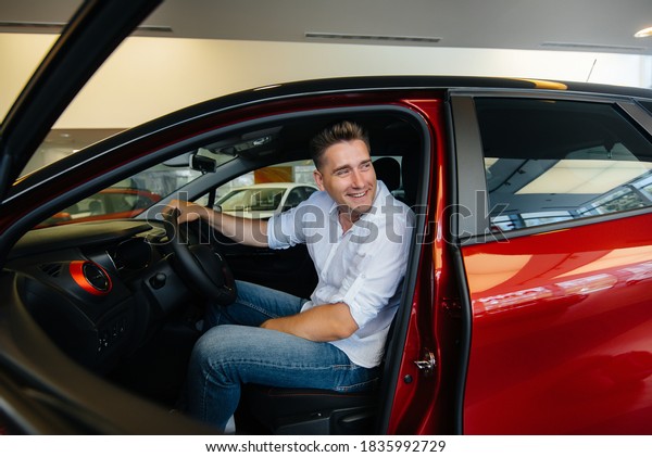 A young man is sitting in the cabin of a new\
car and testing it. Buying a\
car