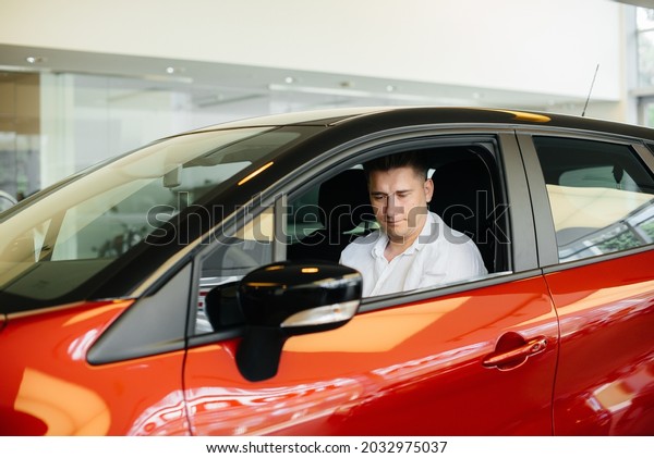 A young man is sitting in the cabin of a new\
car and testing it. Buying a\
car