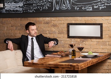 Young Man Sitting In Cafe Waiting For Somebody. Handsome Guy Looking At His Handwatches And Waiting For Girl