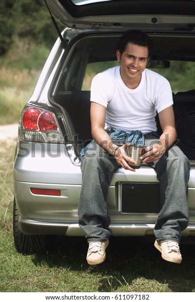 Young man\
sitting in car boot smiling at\
camera