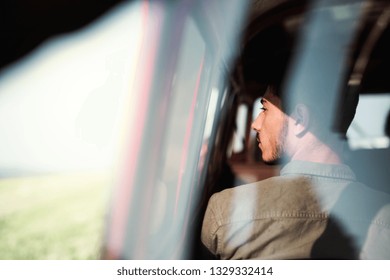 A Young Man Sitting In A Car On Roadtrip Through Countryside, Shot Through Glass.