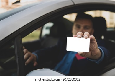 Young Man With Sitting In Car Showing An Empty White Card. Driver Has Got Driving License And Is Very Happy. Parking Pass Or Entrance.