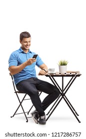 Young Man Sitting At A Coffee Table And Using A Mobile Phone Isolated On White Background