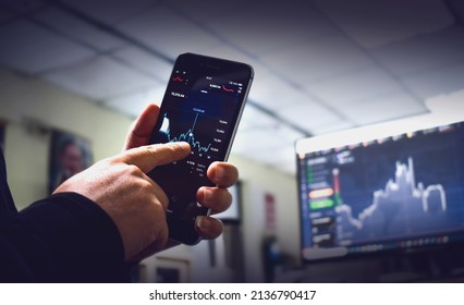 Young man sitting at a computer screen showing a stock chart. Bitcoin chart on the table Work and share computers to trade and modern technology in the digital age and use your phone to trade. - Shutterstock ID 2136790417