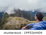 Young man sitting, contemplating Machu Picchu lost city with Huayna Picchu mountain. Ruins of ancient inca civilization in the sacred valley of Cusco Province. Peru, South America