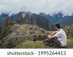 Young man sitting, contemplating Machu Picchu lost city with Huayna Picchu mountain. Ruins of ancient inca civilization in the sacred valley of Cusco Province. Peru, South America