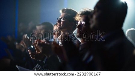 Young Man Sitting in a Crowded Audience at a Business Conference. Male Attendee Cheering and Clapping After a Motivational Keynote Speech. Auditorium with Young Successful Businesspeople.