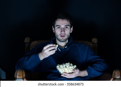 Young Man Sitting In The Dark Room In The Front Of Tv Watching Movie And Eating Popcorn