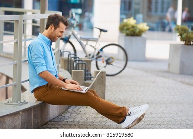 Young Man Sitting With Laptop Outside The Office