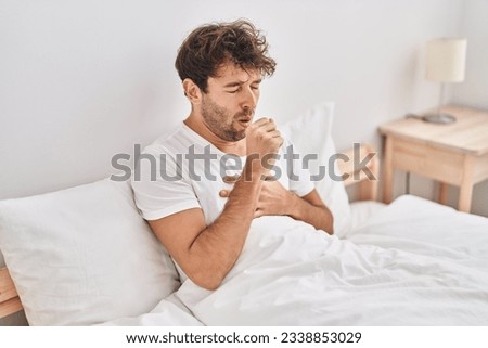 Young man sitting on bed coughing at bedroom