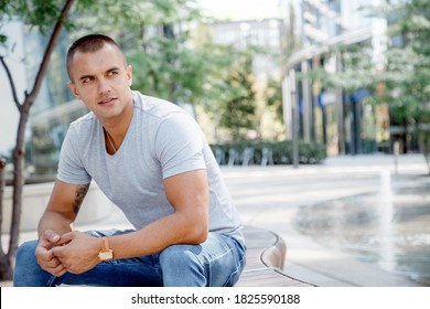 Young man sitting on a bench. The guy in a clear T-shirt and blue pants. The guy on the European Square in Warsaw. Poland.