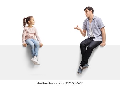 Young man sitting on a blank panel and talking to a child isolated on white background
