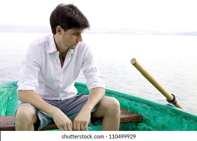 Young man sitting on a boat in a lake thinking expressing sadness