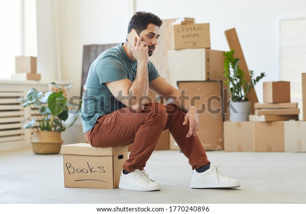 Young man sitting on the box and\
talking on mobile phone he ordering the car for\
relocation