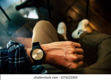 Young man sitting on chair wears a tartan shirt looking at his analog watch on his hand watching the time at the coffee shop. waiting for an appointment.