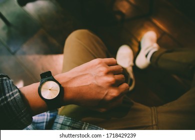 Young man sitting on chair wears a tartan shirt looking at his analog watch on his hand watching the time at the coffee shop. waiting for an appointment. Vintage tone