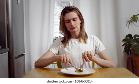 Young Man Sitting On Chair And Eating Tomato And Salad On Plate. Portrait Of Skinny Man Being On Diet Having Vegetables For Dinner. Weight Loss Problem. Starving Young Man Portrait