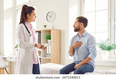 Young man sitting on the couch in the doctor's office and pointing to his chest to the doctor during medical examination in clinic. Physician listening to the patient's complaints. - Powered by Shutterstock