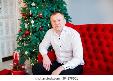 Young Man Sitting On Couch Alone, In Front Of Christmas Tree