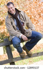 Young man sitting on fence with autumn leaves behind
