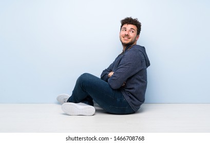Young man sitting on the floor with arms crossed and happy