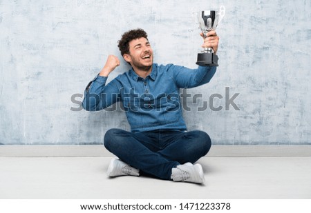 Young man sitting on the floor holding a trophy