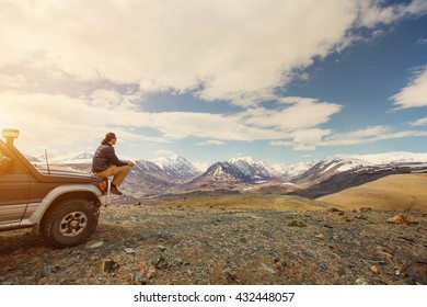 Young man sitting on his car in beautiful mountains landscape. Off-road travel vacation, enjoy  freedom