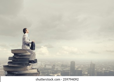 Young man sitting on pile of old books - Shutterstock ID 259794092