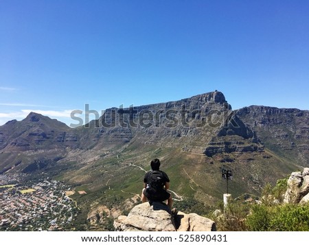 A young man sitting on the rock looking to top view Table Mountain view on on top of Lion 's head in Cape Town, South Africa