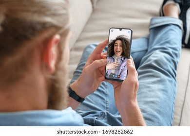 Young man sitting on sofa holding smartphone communicating with african girl friend on mobile screen, making video call using cell phone mobile social media dating app. Video call concept.