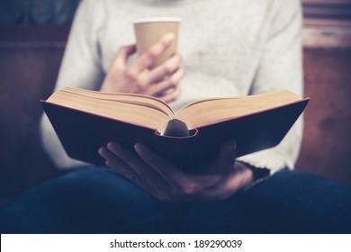Young man is sitting on a sofa and reading a book while holding a paper cup - Shutterstock ID 189290039
