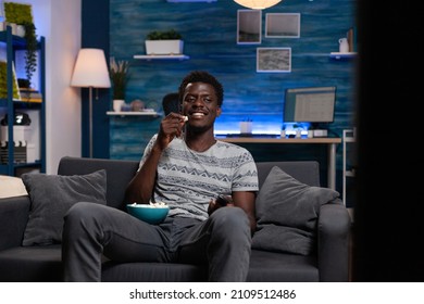 Young man sitting on sofa looking at television watching entertainment movie enjoying lesiure activity at home after busy day. Guy holding popcorn bowl drinking beer during comedy series - Powered by Shutterstock