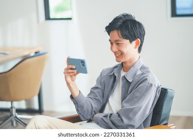 Young man sitting on a sofa watching a video on his smartphone - Powered by Shutterstock