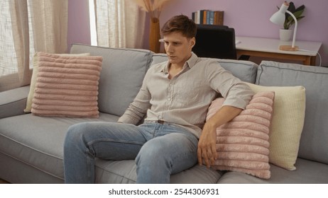 Young man sitting on a sofa in a modern living room with pink and cream cushions, looking contemplative in a cozy home setting. - Powered by Shutterstock