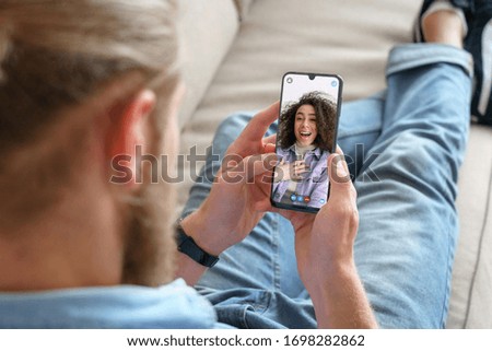 Young man sitting on sofa holding smartphone communicating with african girl friend on mobile screen, making video call using cell phone mobile social media dating app. Video call concept. Stock photo © 