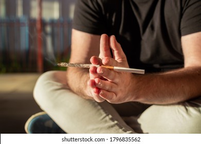 Joven sentado en la calle con una junta de cannabis y un cigarrillo.
