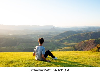 Young man sitting on top of a mountain and looking at the  landscape in the background. Pause to contemplate landscape and nature.