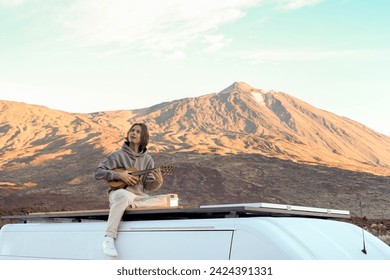 A young man sitting on top of a van in the picturesque Teide Mountain, playing a guitar. - Powered by Shutterstock