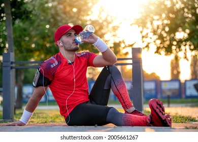 Young Man Sitting Outdoor And Drink Wather After Jogging.